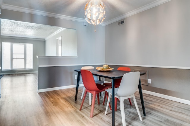 dining space with a textured ceiling, visible vents, light wood-style floors, ornamental molding, and an inviting chandelier