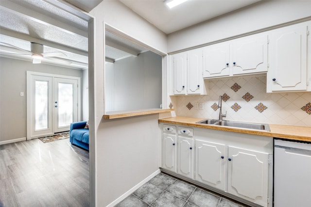 kitchen featuring decorative backsplash, white cabinets, dishwashing machine, french doors, and a sink