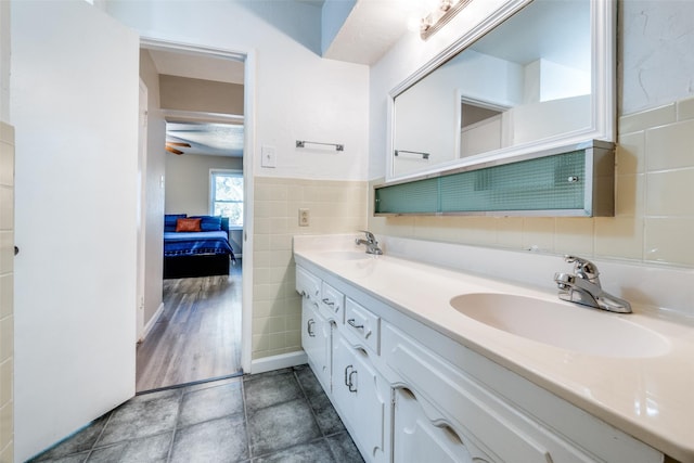 full bathroom featuring double vanity, connected bathroom, tile walls, and a sink