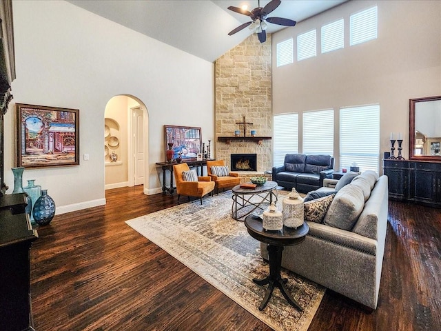 living area with arched walkways, a fireplace, a ceiling fan, wood finished floors, and baseboards