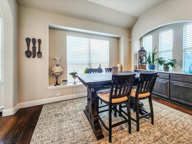 dining space featuring dark wood-style flooring, vaulted ceiling, and baseboards