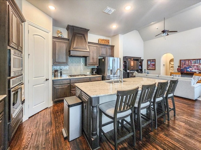 kitchen featuring visible vents, arched walkways, open floor plan, stainless steel appliances, and premium range hood