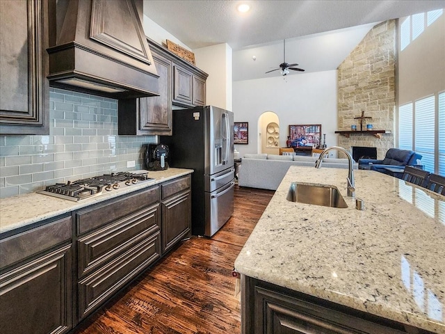 kitchen featuring a stone fireplace, a sink, open floor plan, appliances with stainless steel finishes, and custom exhaust hood