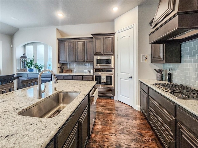 kitchen with dark brown cabinetry, a sink, appliances with stainless steel finishes, custom exhaust hood, and dark wood-style floors