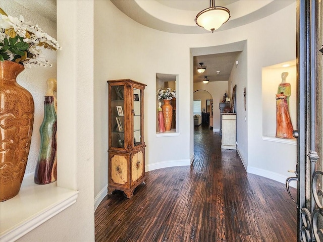 hall featuring arched walkways, wood finished floors, and baseboards