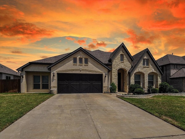 french country home with concrete driveway, a front lawn, an attached garage, and fence