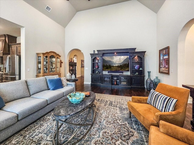 living area with dark wood-style floors, arched walkways, visible vents, high vaulted ceiling, and baseboards