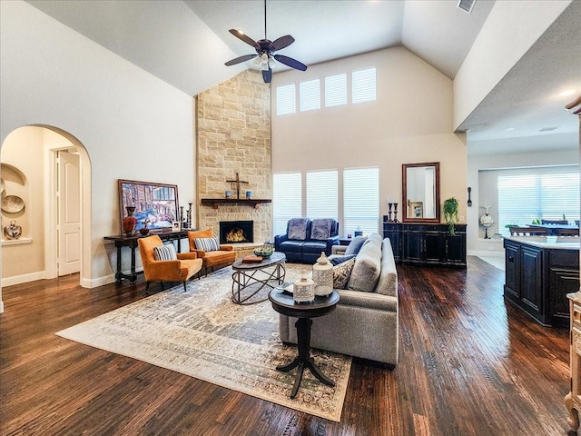 living area featuring arched walkways, ceiling fan, high vaulted ceiling, dark wood-type flooring, and a fireplace