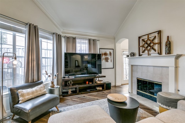 living room with arched walkways, wood finished floors, a tile fireplace, and crown molding