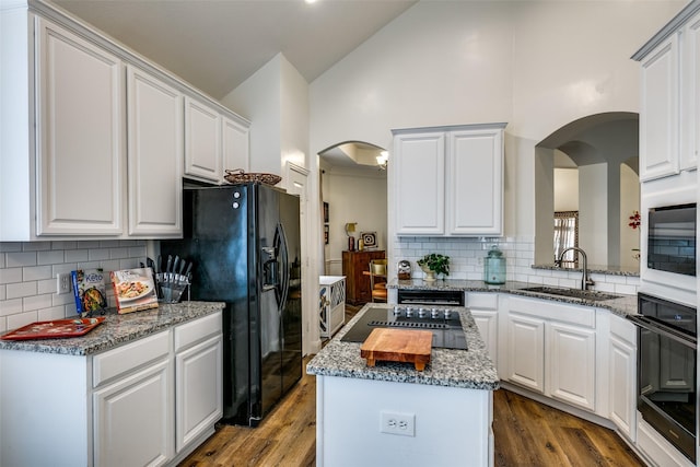 kitchen featuring black appliances, wood finished floors, a sink, and a center island