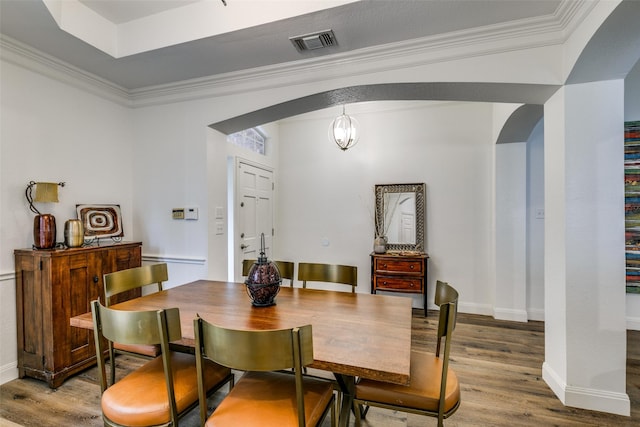 dining room featuring arched walkways, wood finished floors, visible vents, and crown molding