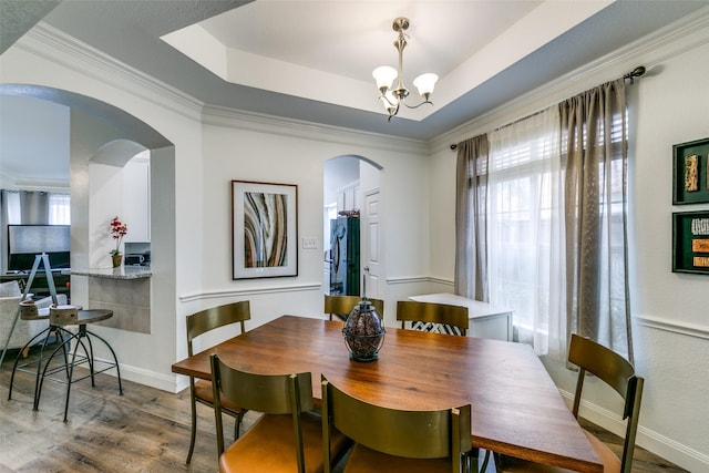 dining room with arched walkways, a raised ceiling, ornamental molding, wood finished floors, and a chandelier