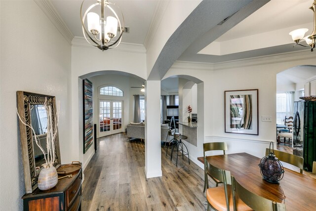 entryway featuring crown molding, arched walkways, a notable chandelier, and wood finished floors