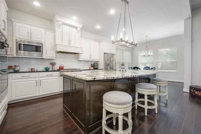 kitchen with a breakfast bar area, stainless steel appliances, custom range hood, decorative backsplash, and an island with sink