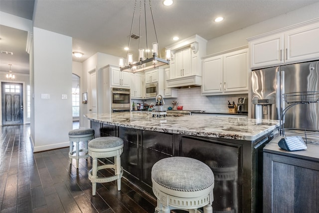 kitchen with dark wood finished floors, custom exhaust hood, decorative backsplash, appliances with stainless steel finishes, and light stone countertops