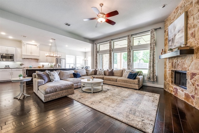 living room with dark wood-style flooring, a fireplace, visible vents, baseboards, and ceiling fan with notable chandelier