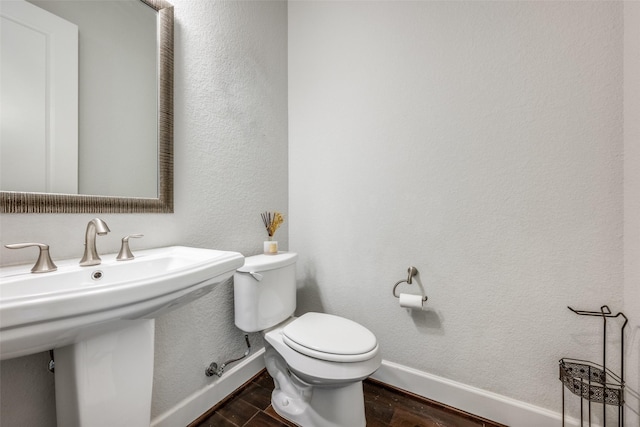 bathroom featuring a textured wall, toilet, a sink, wood finished floors, and baseboards