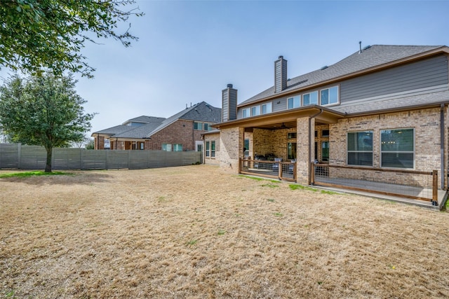 rear view of property with ceiling fan, a patio, brick siding, fence, and a chimney