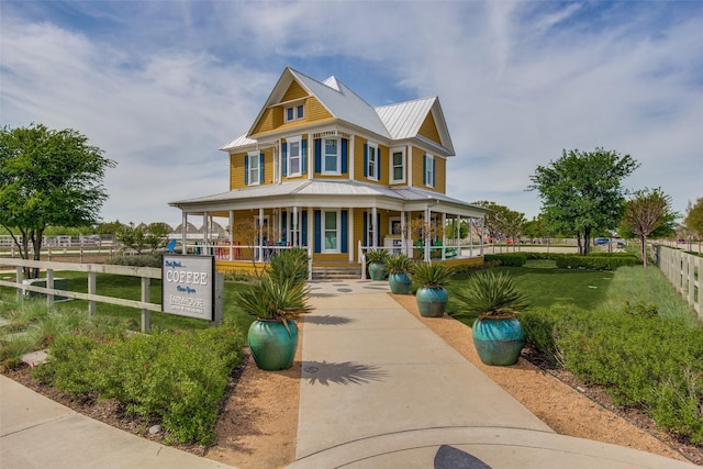 view of front of home featuring concrete driveway, metal roof, covered porch, fence, and a front yard