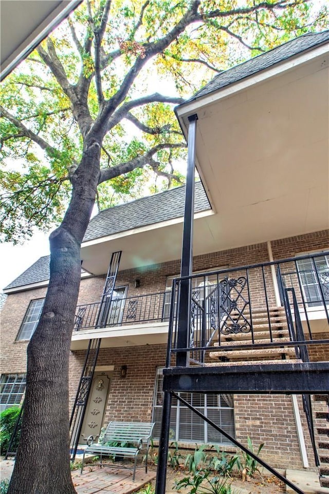 back of house with a balcony, roof with shingles, and brick siding