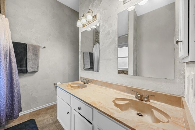 bathroom with a textured wall, double vanity, a sink, and baseboards