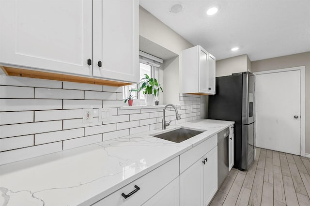 kitchen featuring stainless steel appliances, a sink, white cabinetry, backsplash, and light wood finished floors