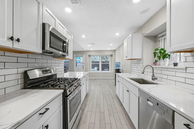 kitchen with light wood finished floors, appliances with stainless steel finishes, white cabinets, and a sink