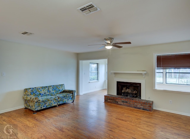 living area featuring a brick fireplace, wood finished floors, visible vents, and baseboards