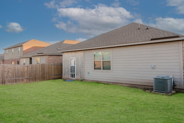 back of property featuring a shingled roof, fence, cooling unit, and a yard