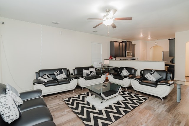 living room featuring light wood finished floors, visible vents, arched walkways, and a ceiling fan