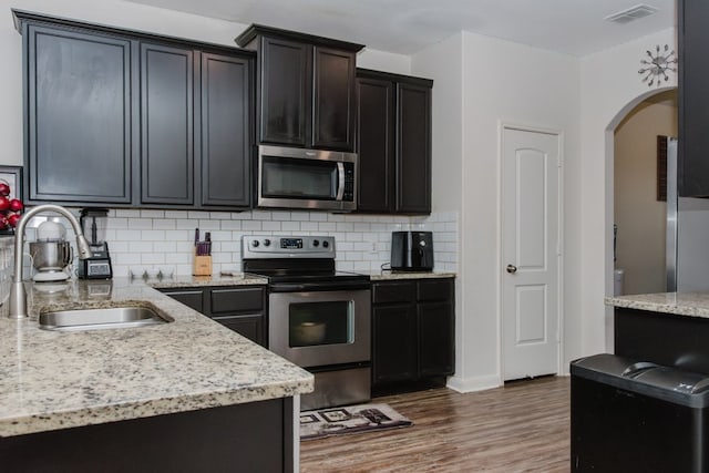 kitchen featuring arched walkways, a sink, visible vents, appliances with stainless steel finishes, and decorative backsplash