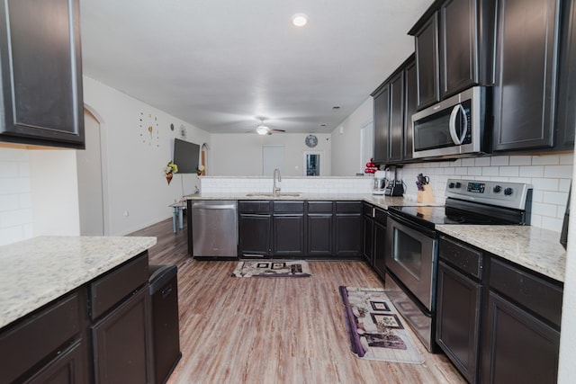 kitchen featuring a peninsula, a sink, appliances with stainless steel finishes, backsplash, and light wood finished floors