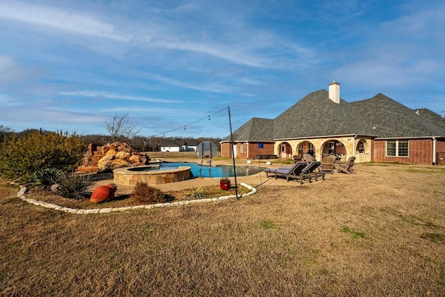 rear view of house with brick siding, a patio, a chimney, a pool with connected hot tub, and a lawn