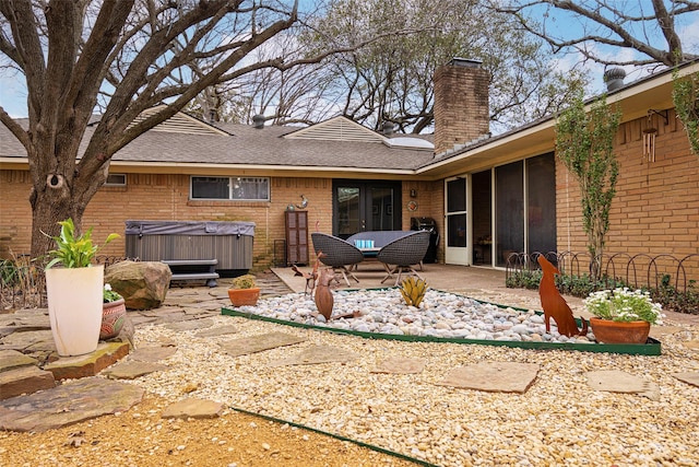 back of property with brick siding, a chimney, a patio area, and a hot tub