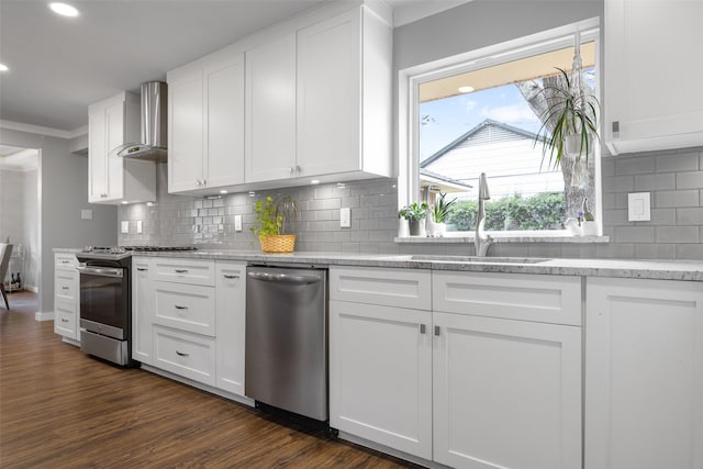 kitchen with white cabinets, appliances with stainless steel finishes, dark wood-type flooring, wall chimney range hood, and a sink