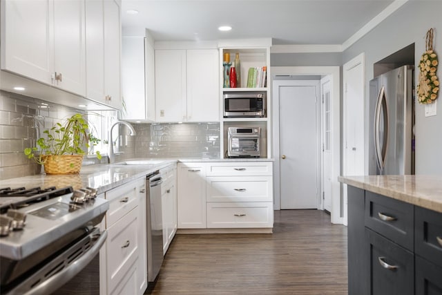 kitchen with light stone counters, stainless steel appliances, a sink, white cabinetry, and dark wood finished floors