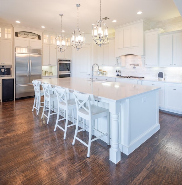 kitchen featuring appliances with stainless steel finishes, dark wood-type flooring, a large island with sink, and white cabinets