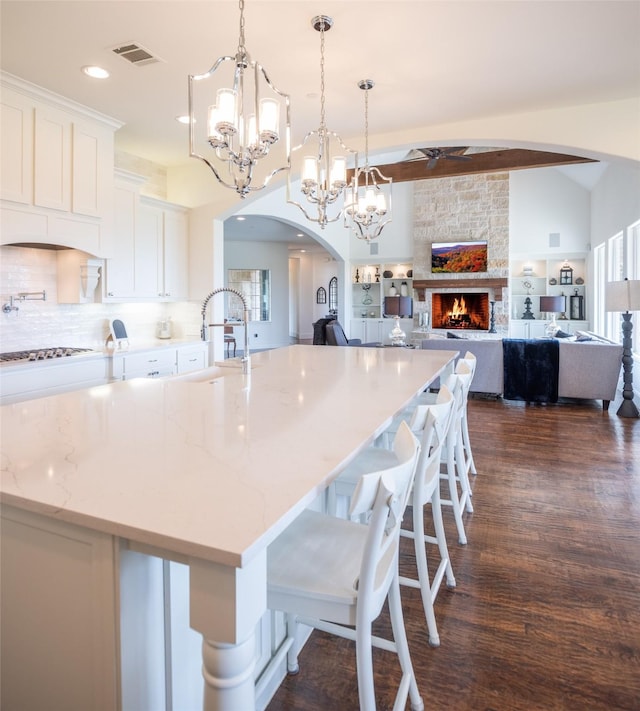 kitchen with arched walkways, a stone fireplace, dark wood-type flooring, white cabinetry, and stainless steel gas stovetop