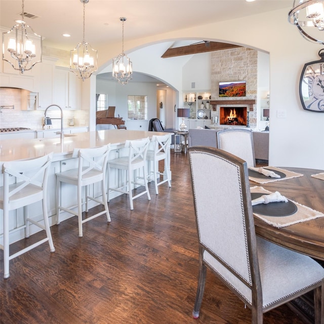 dining area featuring arched walkways, a stone fireplace, dark wood-type flooring, visible vents, and vaulted ceiling