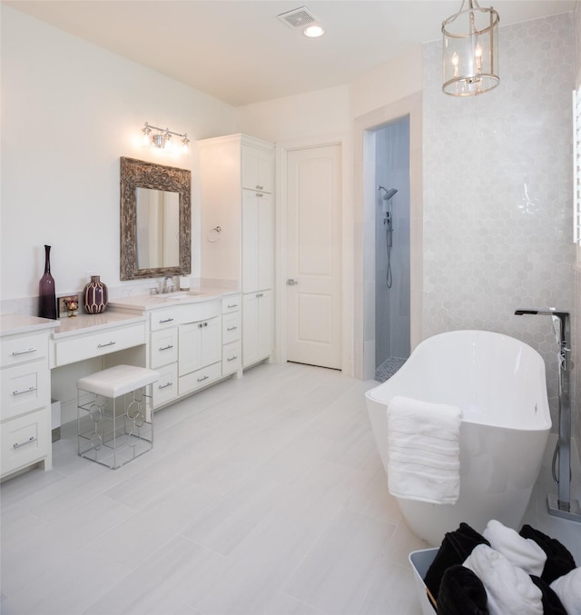 full bathroom with tile walls, visible vents, vanity, a freestanding tub, and tiled shower