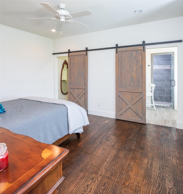 unfurnished bedroom featuring ceiling fan, a barn door, connected bathroom, wood finished floors, and baseboards