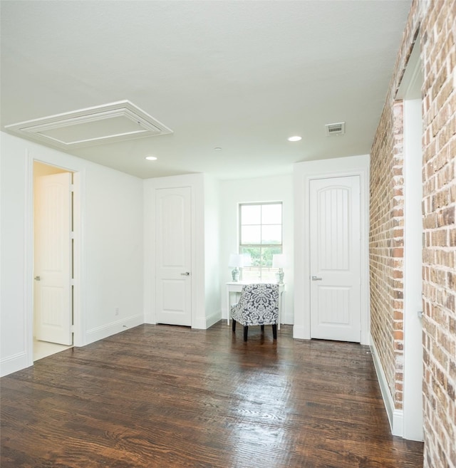 empty room with brick wall, wood finished floors, visible vents, baseboards, and attic access