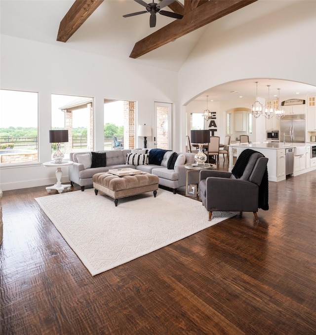 living room featuring baseboards, arched walkways, dark wood-style flooring, high vaulted ceiling, and beam ceiling