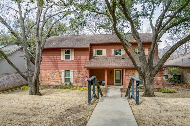 view of front facade with roof with shingles and brick siding