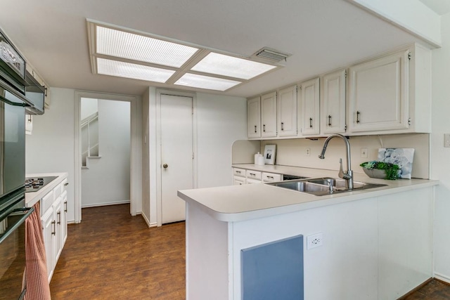 kitchen featuring dark wood finished floors, light countertops, a sink, a peninsula, and black appliances