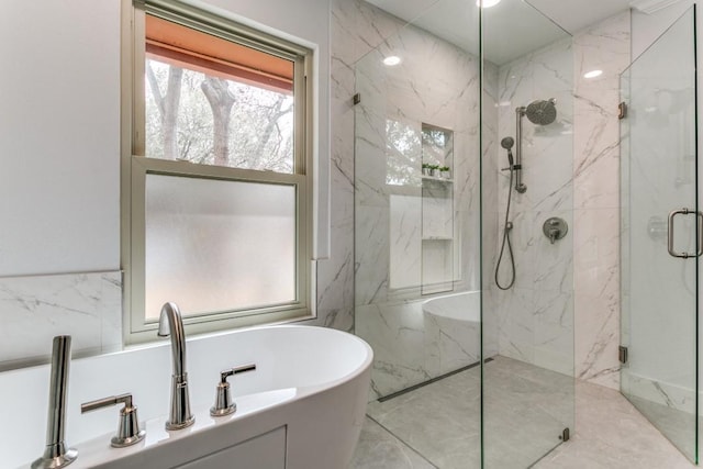 bathroom with marble finish floor, a freestanding tub, a marble finish shower, and tile walls