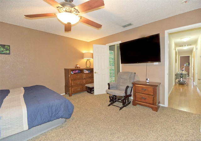 carpeted bedroom featuring a ceiling fan, visible vents, and a textured ceiling