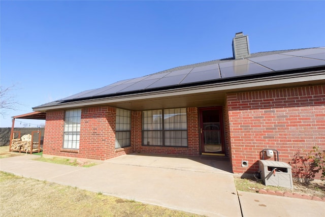 entrance to property featuring roof mounted solar panels, brick siding, and a chimney