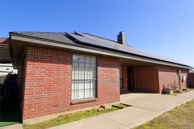 view of home's exterior featuring a chimney, solar panels, and brick siding