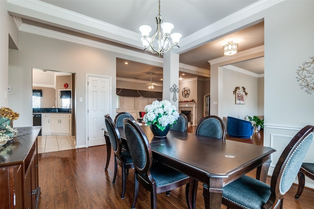 dining room featuring dark wood-style floors, a fireplace, ornamental molding, and ceiling fan with notable chandelier